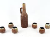 un vase marron et six petites tasses devant celui-ci