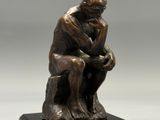 une statue en bronze représentant un homme assis sur un socle en bois