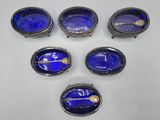 six blue glass bowls with spoons and spoon rest on a white surface