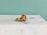 une image représentant une bague en or sertie d'une citrine facettée, posée sur une dalle de marbre