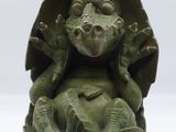 une sculpture verte représentant une grenouille assise sur un œuf