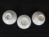 three white porcelain cups and saucers sitting on a black cloth