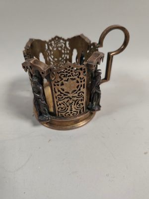 une image représentant une petite tasse en métal munie d'une anse, posée sur une surface blanche