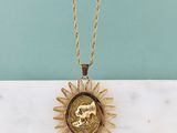 un collier en or orné d'un soleil rayonnant, posé sur une surface en marbre