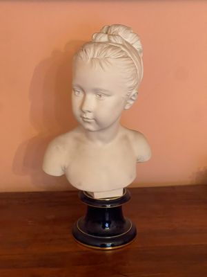 a white bust of a young girl on a wooden table
