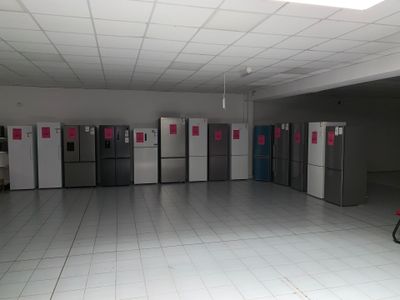 Plusieurs réfrigérateurs sont alignés dans une grande pièce au sol carrelé de blanc.