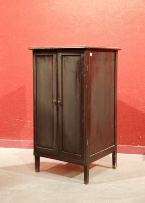 une petite armoire dans un coin d'une pièce, avec un mur rouge en arrière-plan