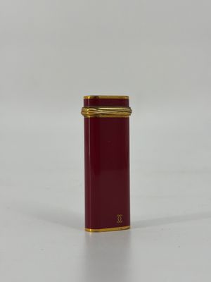 une image représentant un récipient rouge et doré posé sur une surface blanche