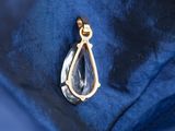 a close up of a blue shirt with a gold tear shaped pendant
