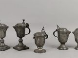 quatre tasses en argent sont alignées les unes à côté des autres sur une surface blanche
