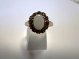 une image représentant une bague ornée d'une pierre blanche entourée de grenats
