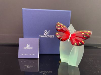 une sculpture en verre représentant un papillon rouge posé sur une table noire