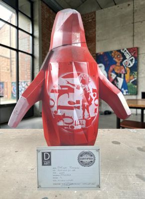 une statue de pingouin rouge posée sur une table devant une fenêtre