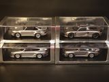 three silver die cast cars in clear boxes on a black surface