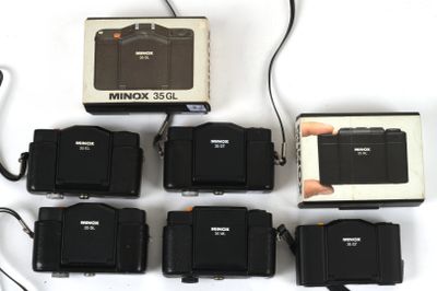 six cameras and a box of batteries on a white surface