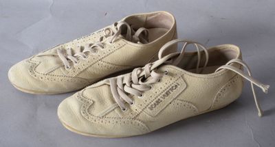une paire de chaussures en cuir beige à lacets posée sur une surface grise