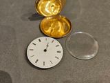 une montre de poche en or posée sur une table, à côté d'une loupe