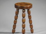 un petit tabouret en bois aux pieds tournés, sur fond gris