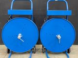deux bobines en acier bleu posées sur des roulettes, adossées à un mur noir