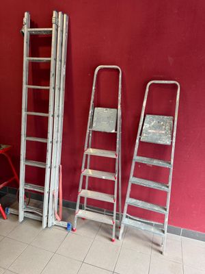 Plusieurs échelles sont alignées contre un mur rouge dans une pièce.