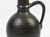 a black vase with a brown handle sitting on a white surface