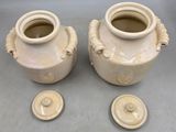pair of cream colored vases with handles and lids on a gray surface