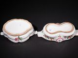 two white dishes with gold trim on them on a black surface