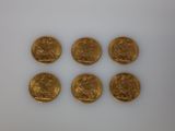 six gold coins sitting on top of each other on a white surface