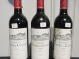 trois bouteilles de vin posées sur une table, à côté d'une horloge