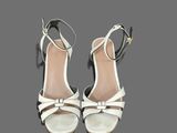 a pair of women ' s white sandals with a bow on the heel