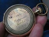 Quelqu'un tient dans sa main une montre de poche sur laquelle est gravé un nom.