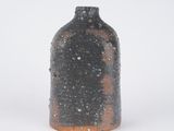 a black vase with a brown base on a white surface