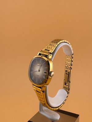 une montre en or posée sur un socle, sur une surface marron