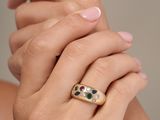 a woman wearing a gold ring with green and red stones