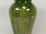 un vase vert posé sur une surface blanche