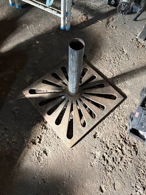 un siphon de sol en métal posé à même le sol, à côté d'une échelle