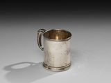 une vieille coupe en argent munie d'une anse, posée sur une surface blanche