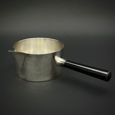 une casserole en argent avec une poignée noire posée sur une table noire