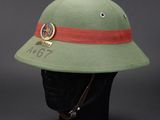 an army green helmet with a red band and a badge on it