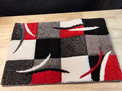 un tapis posé au sol, orné d'un motif rouge, noir et blanc