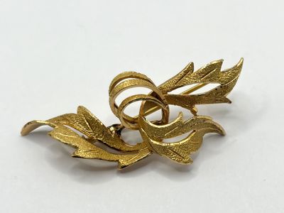 a close up of a gold brooch with leaves on it