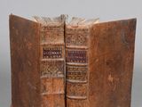 two old books sitting on top of each other on top of a table