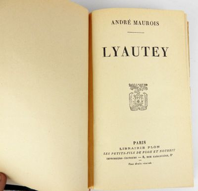 un livre ouvert posé sur une table, avec une main tenant un stylo
