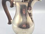 an antique silver coffee pot with a wooden handle sitting on a table