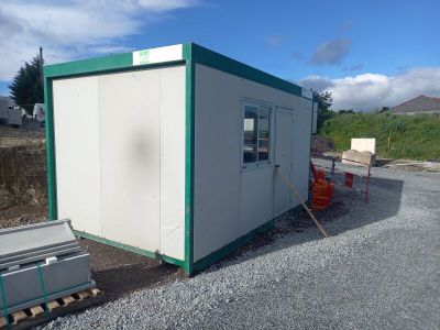 a small white building with a green roof on a gravel lot