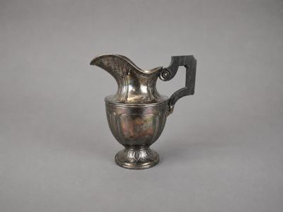 an old silver pitcher with a handle on a gray background