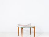 une table avec un plateau en verre et des pieds en bois dans une pièce blanche