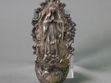 a silver statue of the virgin of guadalupe on a glass stand