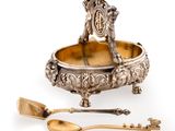 an antique silver plate with a spoon and spoon rest on a white surface