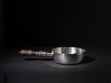 an old metal bowl with a wooden handle on a black surface